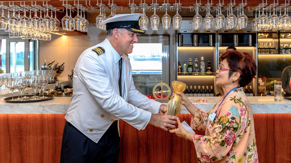 Senior Master Gary Wilson presenting Coral Adventurer's Godmother Mrs Quek Peck Lim with the ceremonial champagne